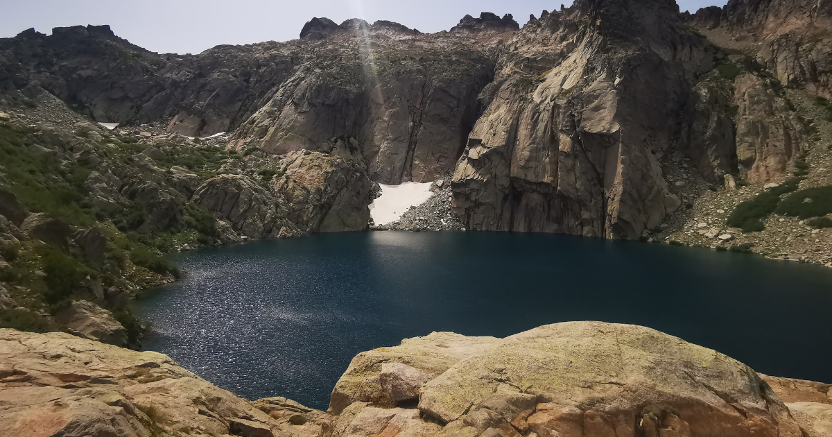 Le lac de Melo vu depuis les rochers, névé et falaises granitiques en arrière-plan